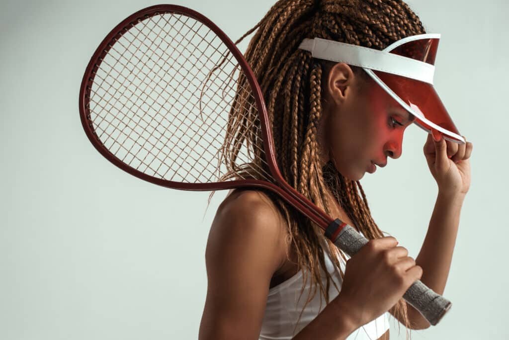 Sporty and beautiful. Side view of young african woman in sports clothes holding tennis racket on