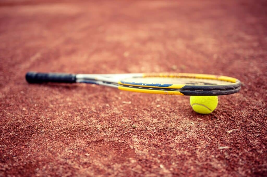 Close-up of tennis racket and ball on clay tennis court