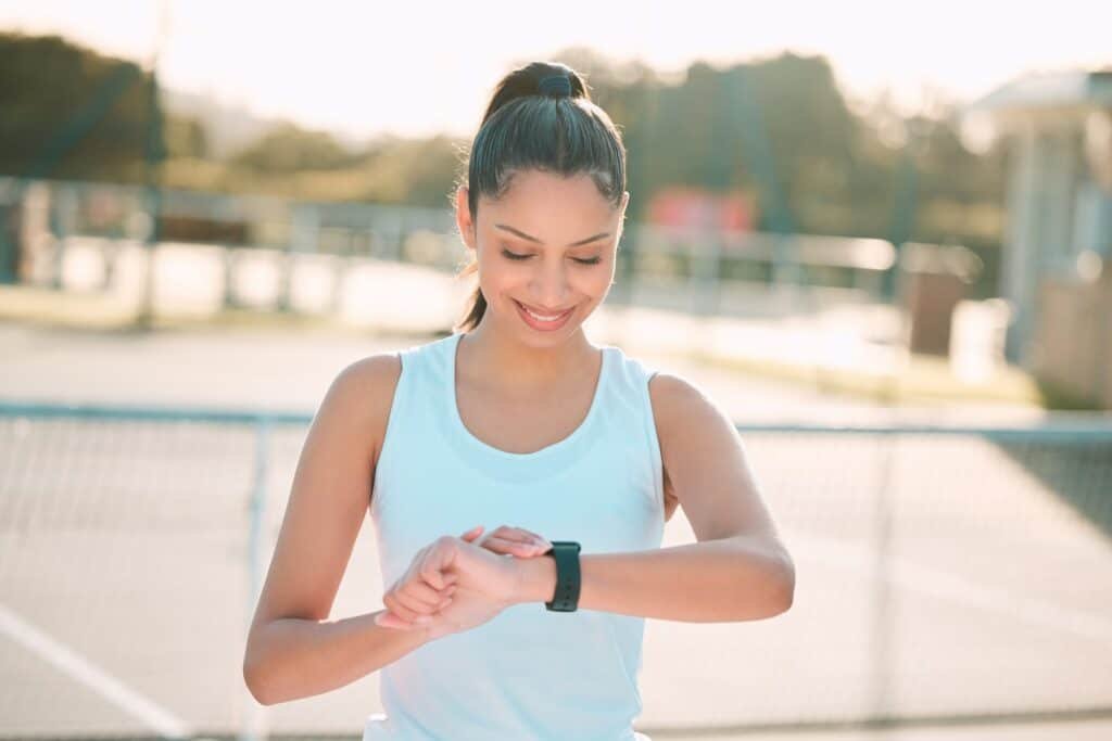 Shot of an attractive young woman standing alone and checking her watch during tennis practise