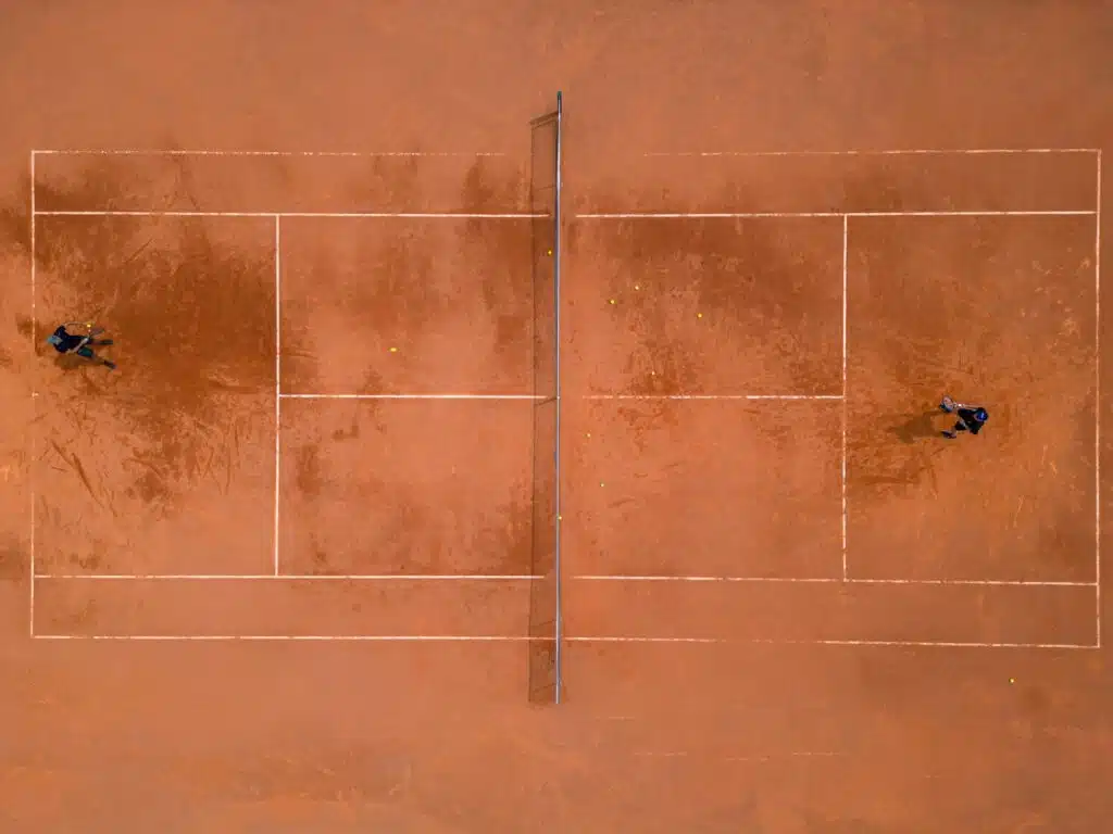 A panoramic view from above captures a tennis training session. The players on the court are focused