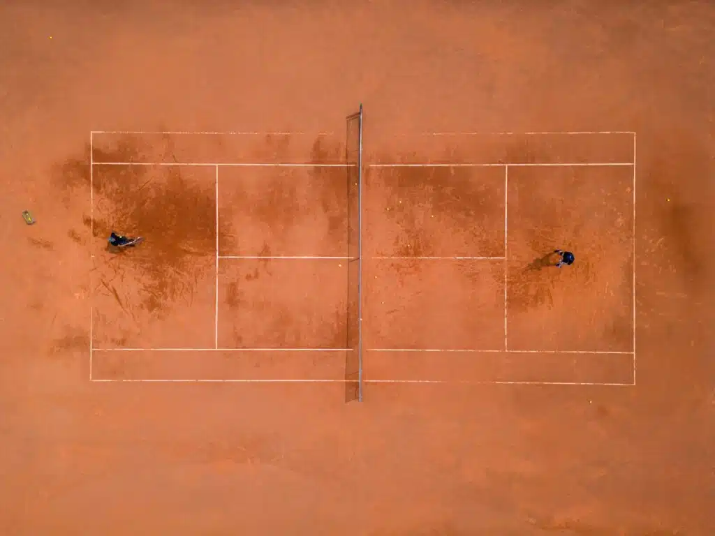 A panoramic view from above captures a tennis training session. The players on the court are focused
