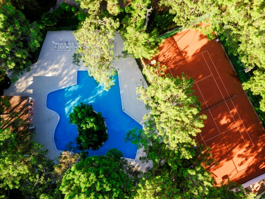 Aerial photography of Clay Tennis Court Complex on Sunny Day surrounded by Green Forest