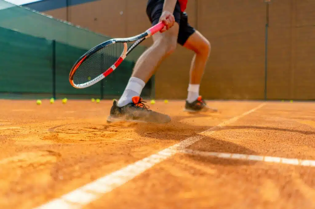 close-up of a tennis player's or instructor's foot on an outdoor court ground dust rising