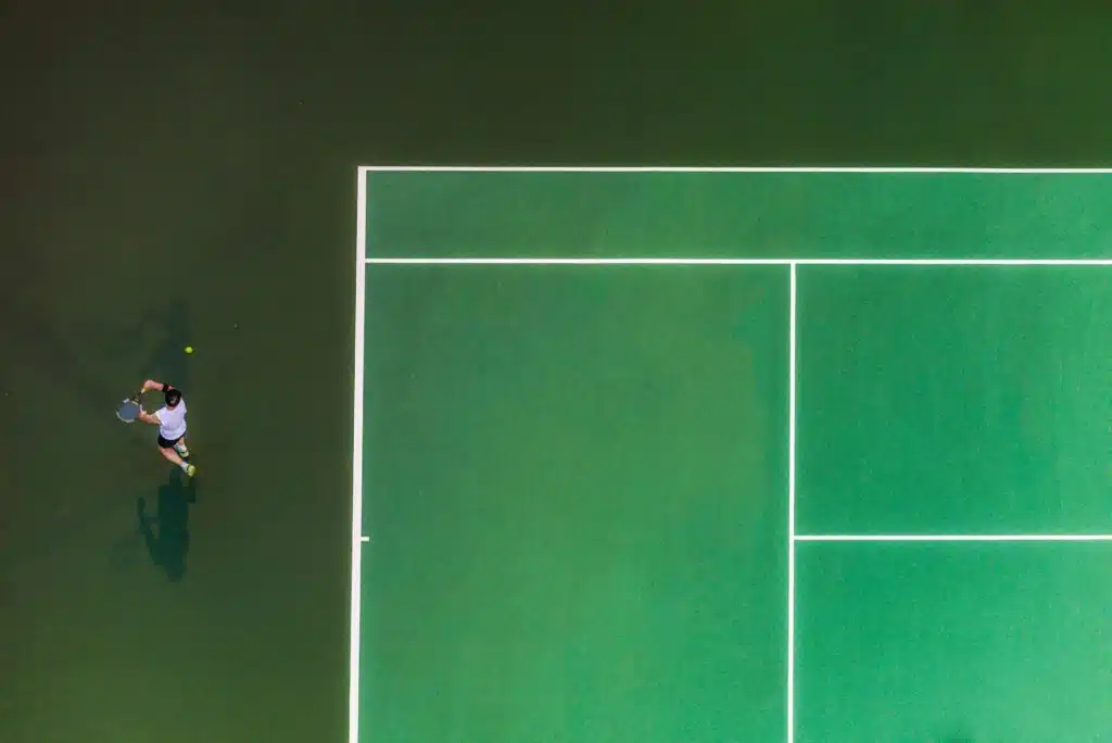 Looking down at a tennis player attempting a one handed-backhand stroke.